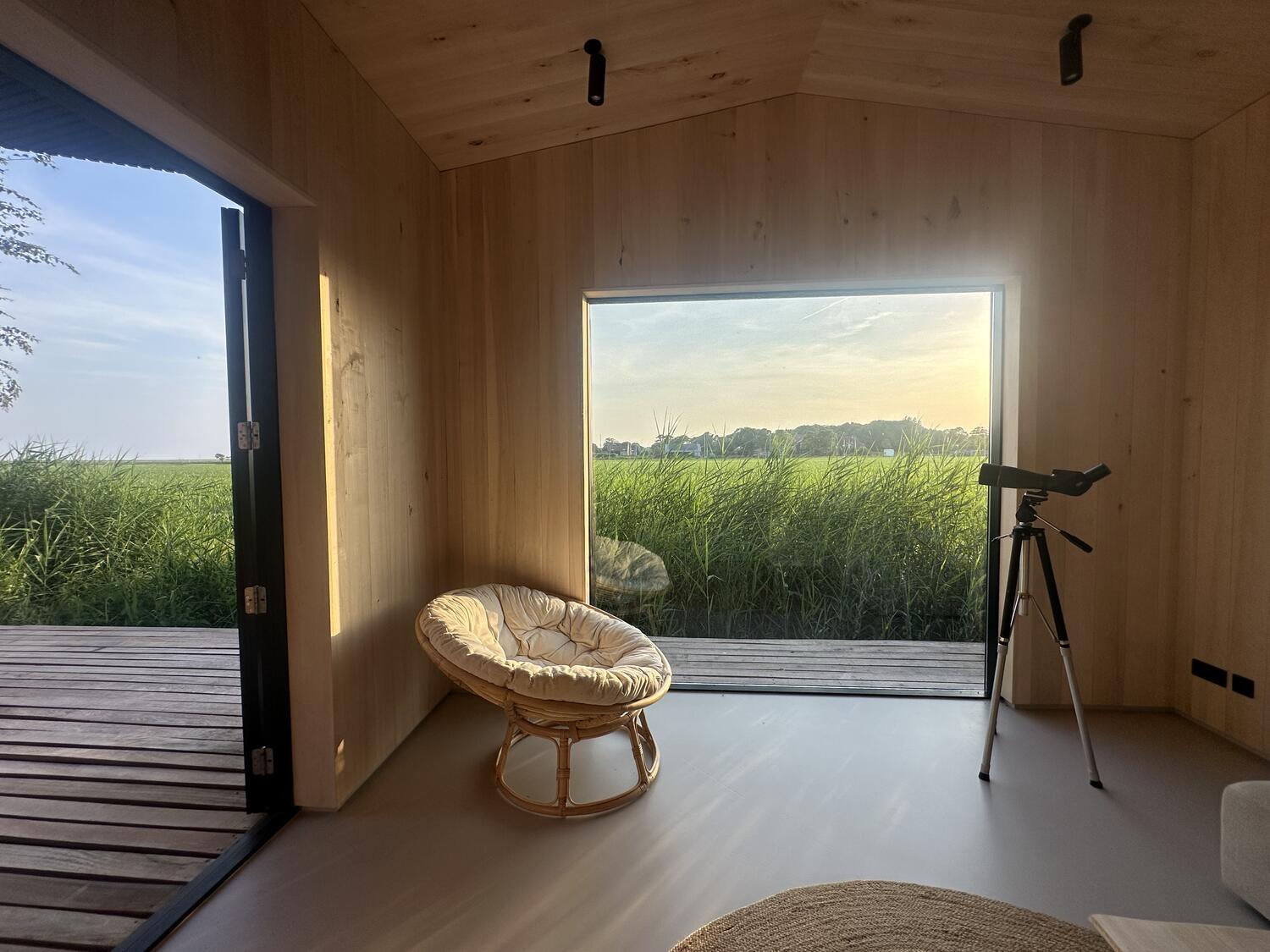 Zwart houten vakantiehuis aan de rand van een rietveld op Schiermonnikoog bij zonsondergang
