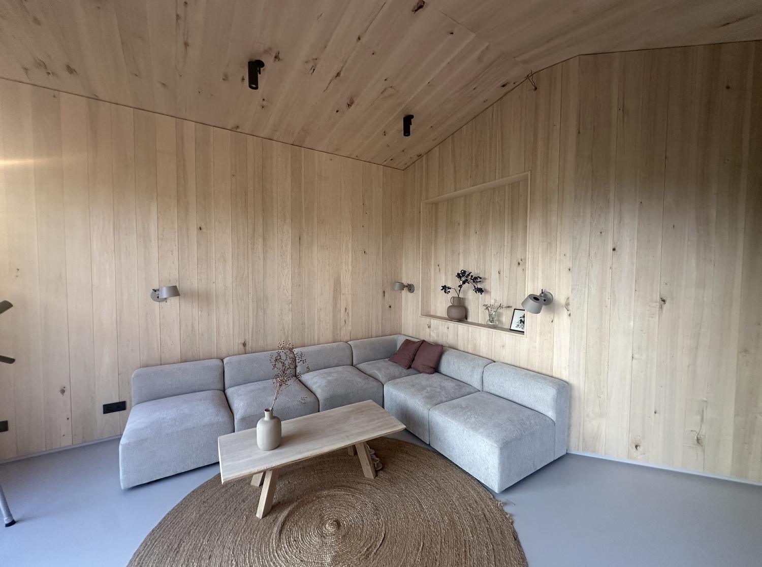 Lichte houten woonkamer met grijze modulaire hoekbank, jute vloerkleed en houten salontafel